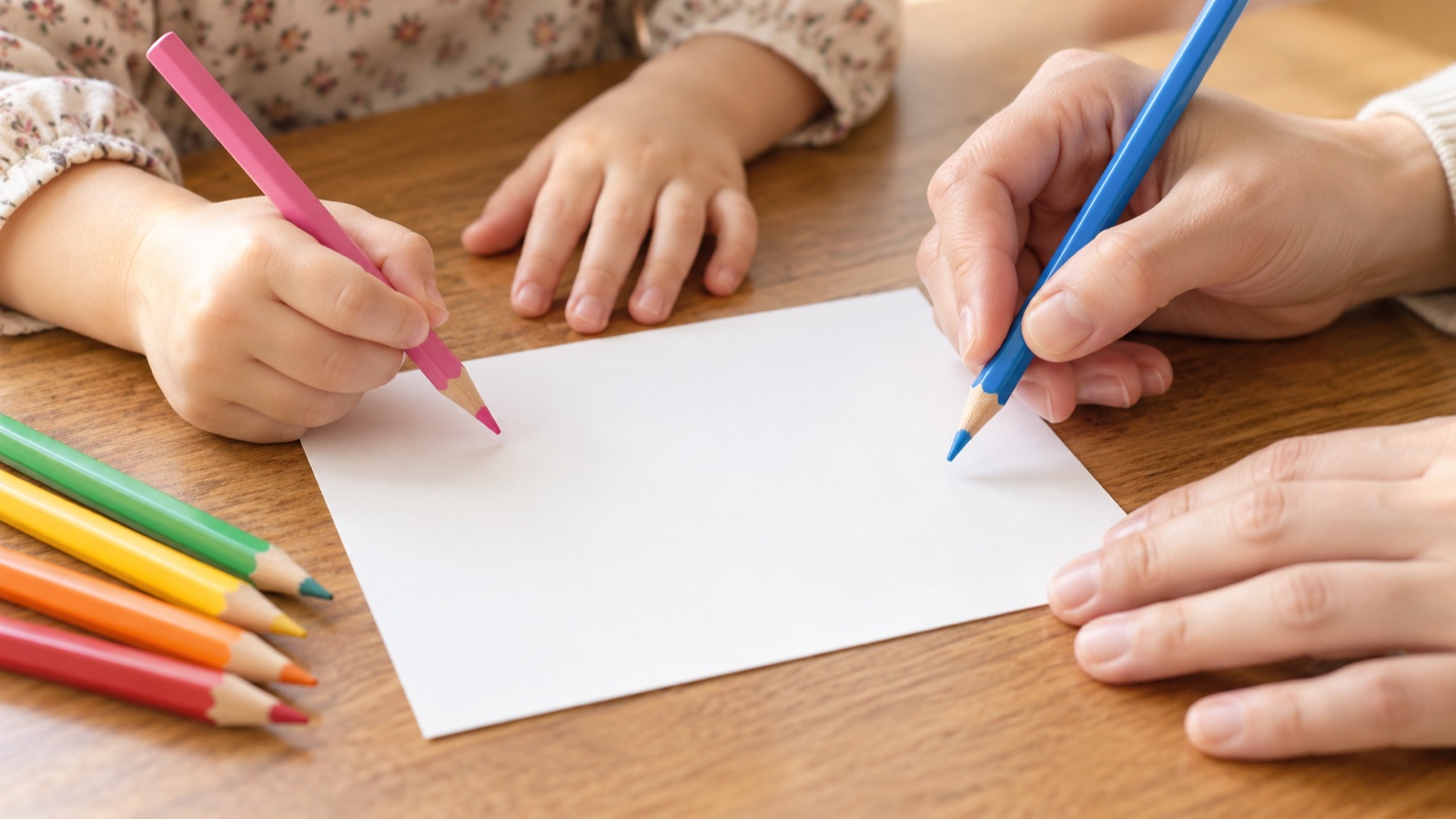 無地のはがきに色えんぴつで絵をかこうとする親子の手元(イメージ)